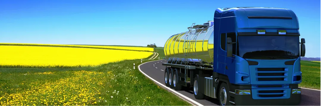 Blauer Tanklastzug auf Landstraße neben blühendem Rapsfeld als Symbol für Biokraftstoff und HVO-Heizöl